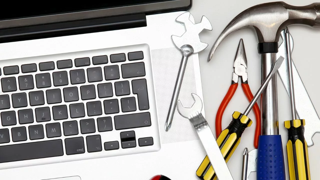A laptop computer sitting on a desk with various tools and devices next to it, including a screwdriver, a wrench. The tools symbolise the importance of regular maintenance and updates for a WordPress website to keep it running smoothly.